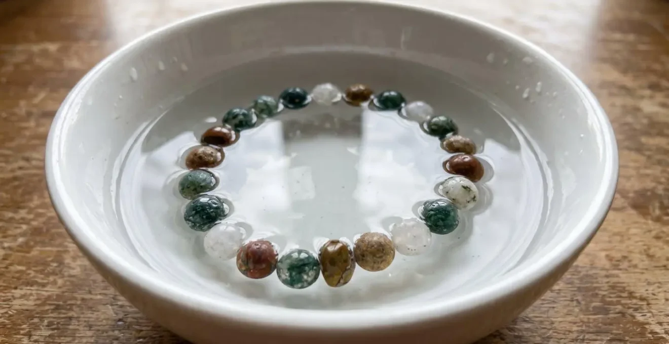 Bracelet en pierres naturelles plongé dans un bol d'eau claire, avec des gouttes sur les pierres